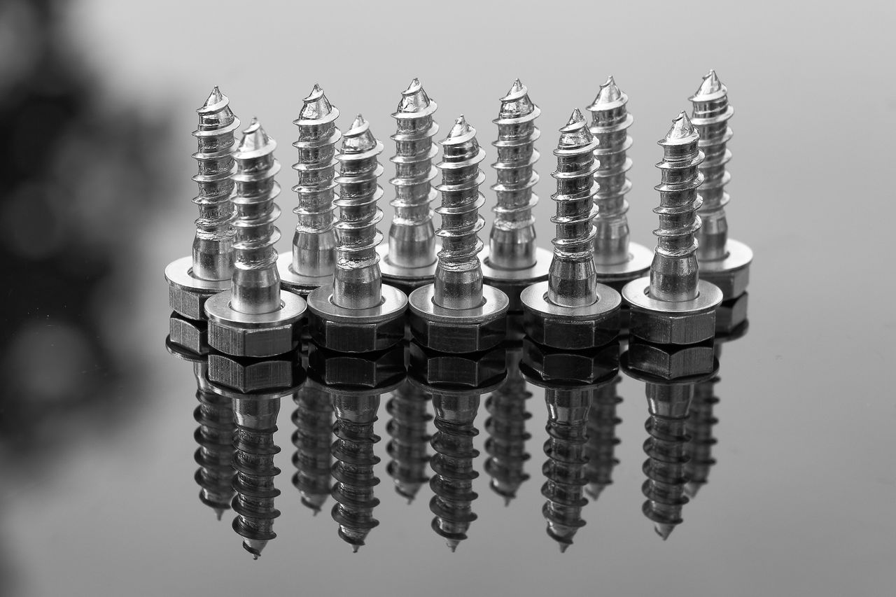 Close-up of shiny metal screws reflecting on a glossy surface. Ideal for industrial or construction themes.